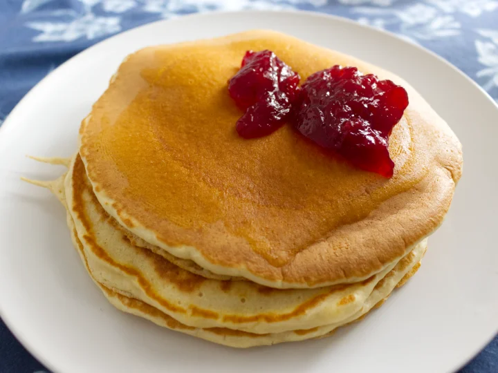 Stack of american style pancakes, topped off with a heaping helping of strawberry jam.